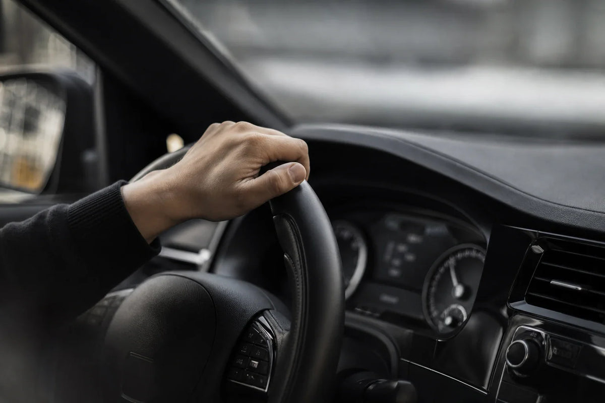 Driver holding a steering wheel inside a clean dark car cabin.